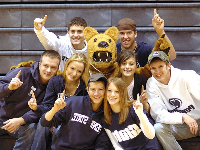 Various students sitting with the Nittany Lion mascot and holding up their index fingers as if to say, “We’re number one!”